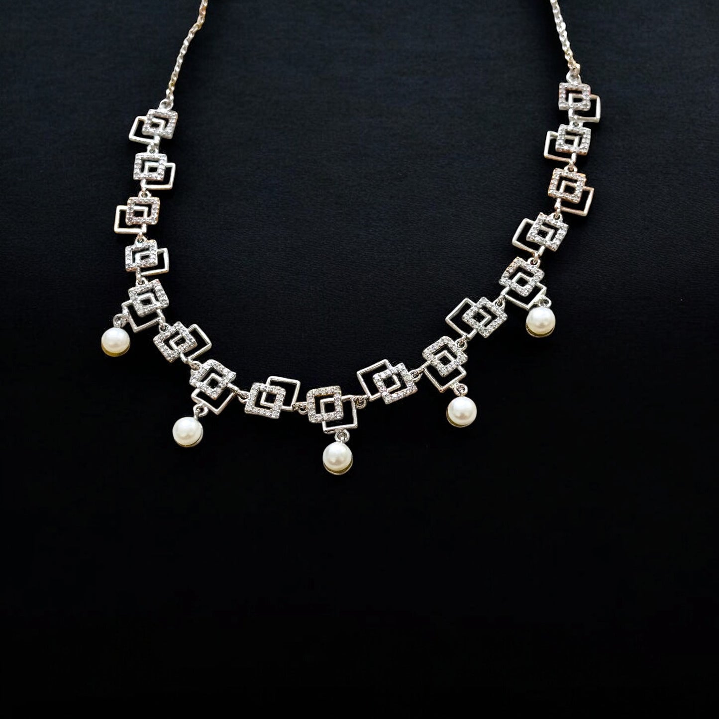 Silver necklace with geometric design and pearl-like beads on a black background
