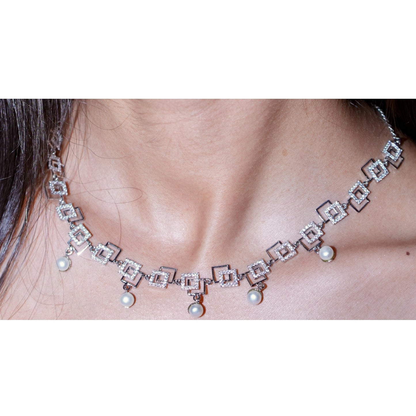 Necklace with square pendants and pearls on a person's neck against a white background