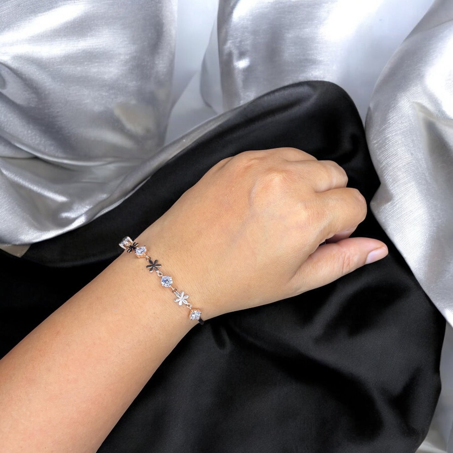 Hand wearing a bracelet with floral designs against a black and silver background