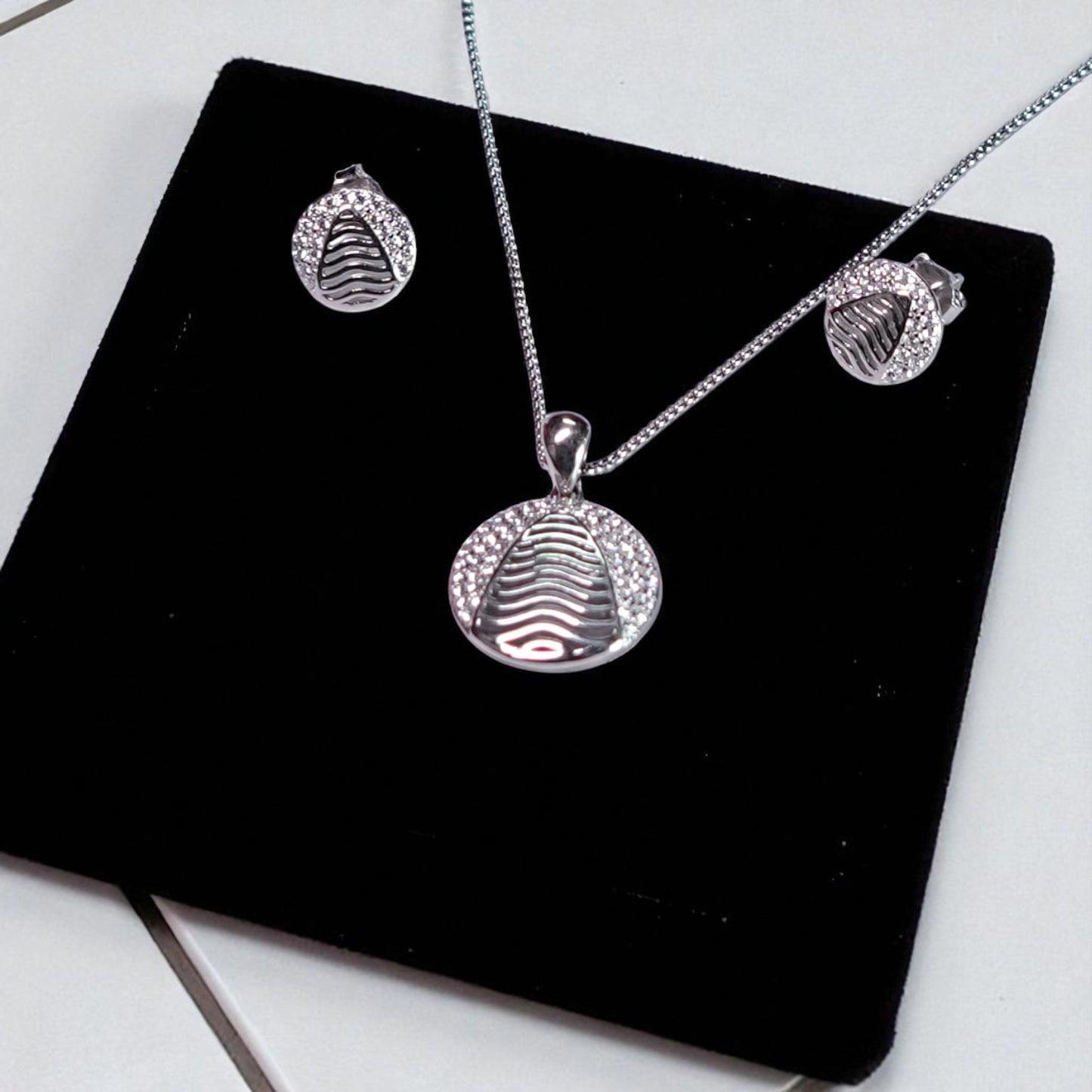 Silver jewelry set with pendant, necklace, and earrings on a black display stand.