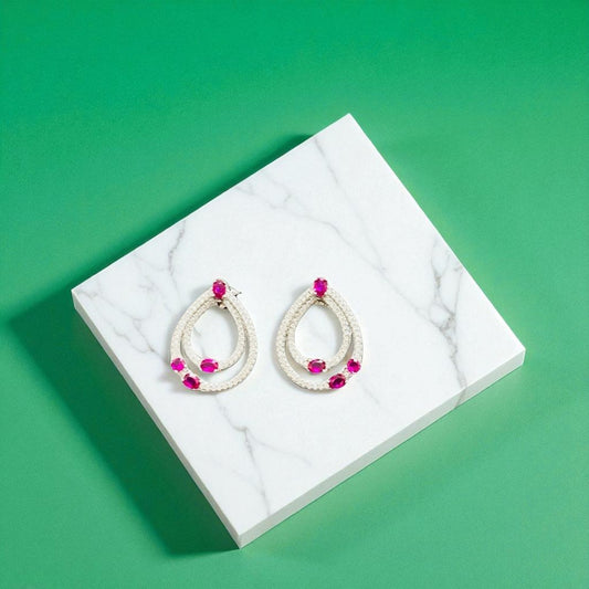 Pair of earrings on a white marble stand against a green background