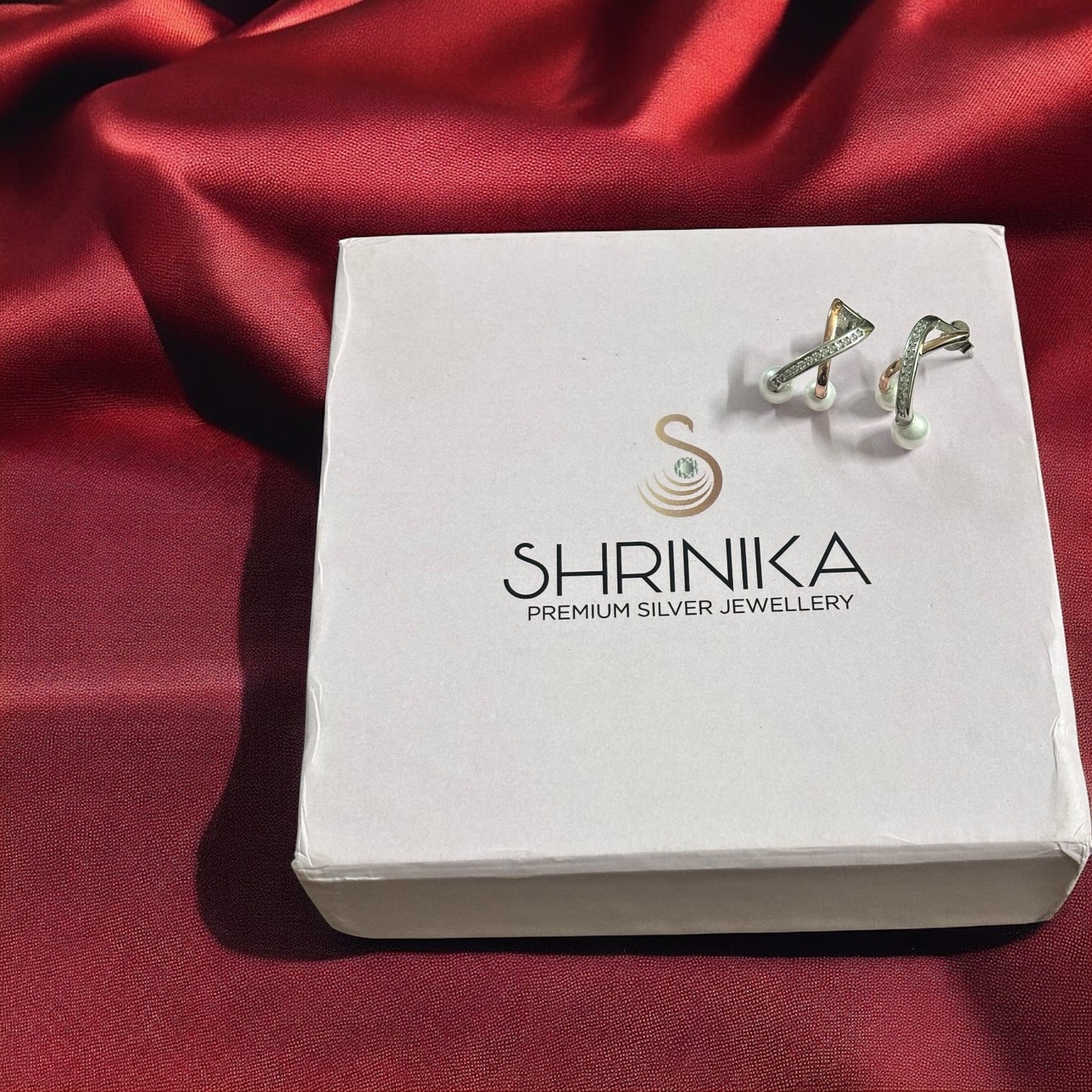 Silver earrings on a Shrinika branded box against a red satin background