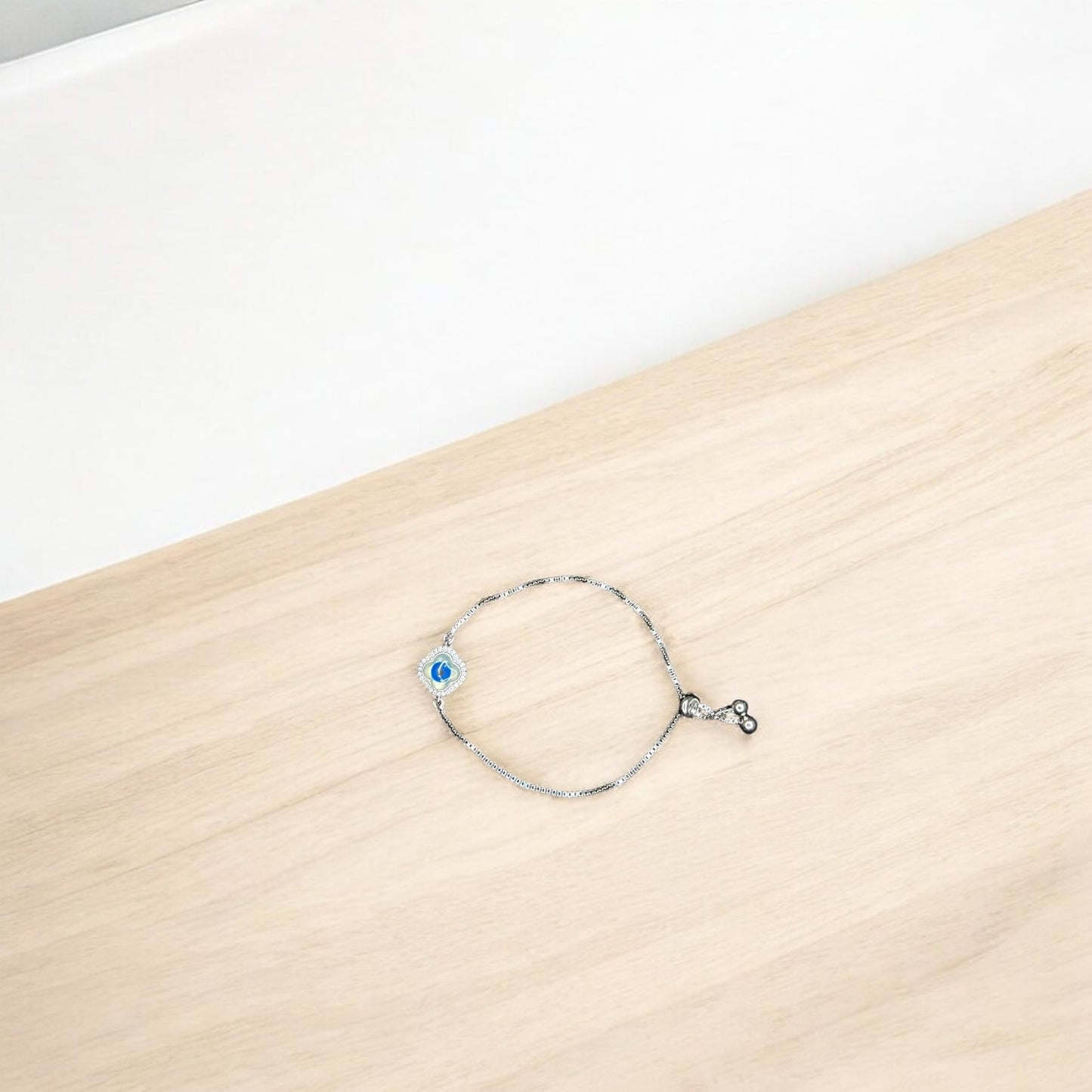 Silver bracelet with a blue evil eye charm on a wooden surface