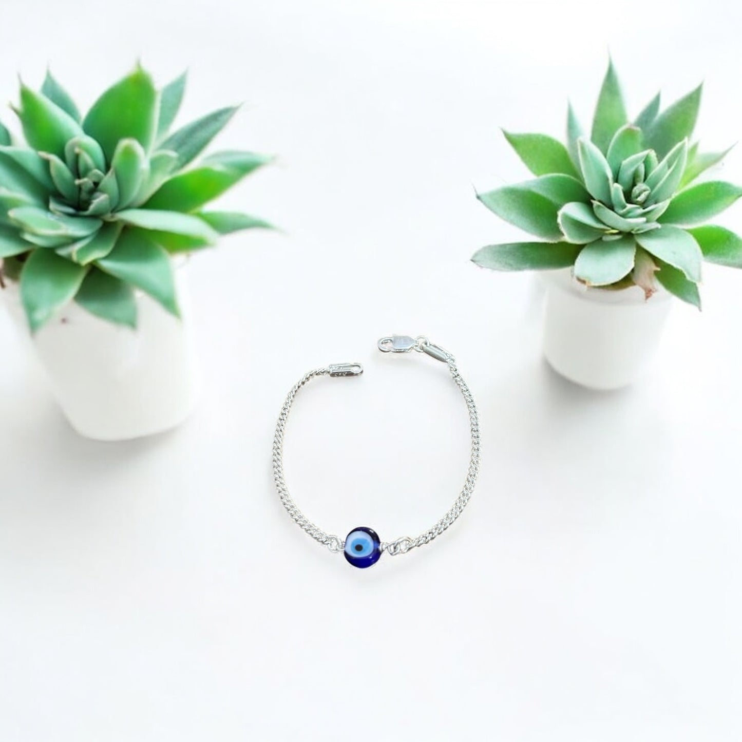 Silver bracelet with a blue evil eye charm on a white background with two succulents.