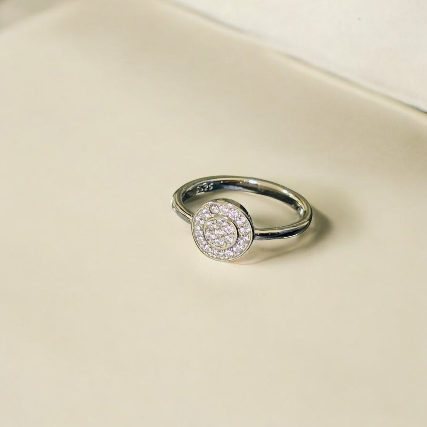 Silver ring with a circular gemstone on a beige background