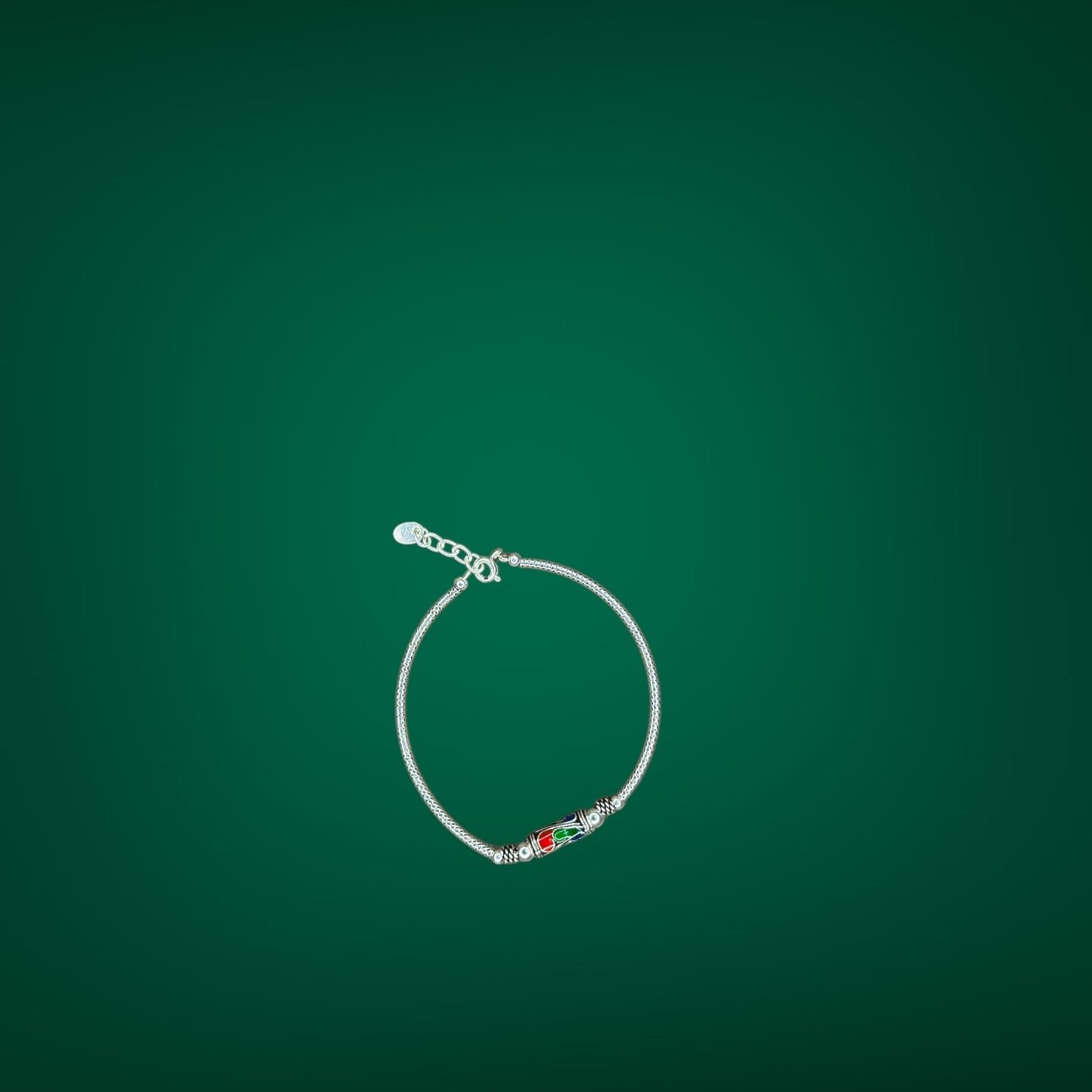 Silver bracelet with a red and green charm on a green background