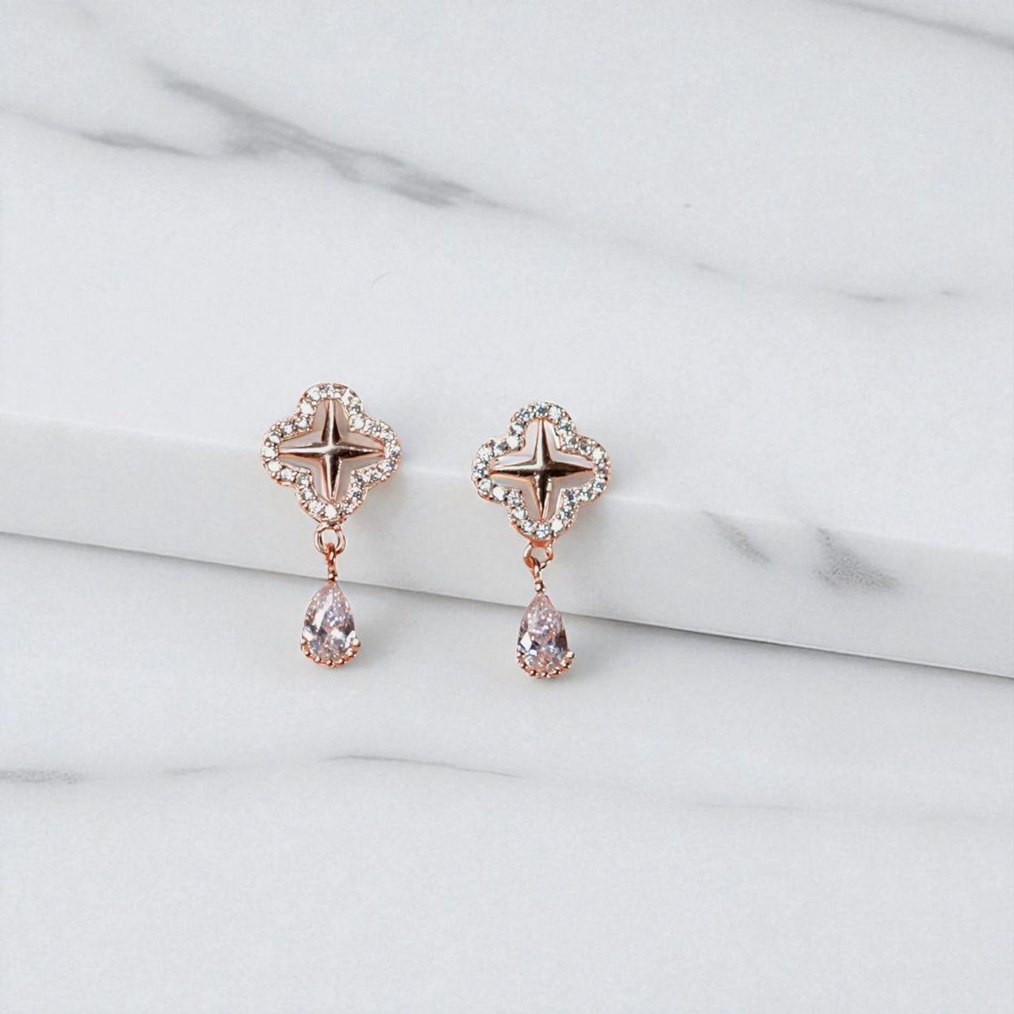 Rose gold earrings with star and teardrop designs on a light gray background