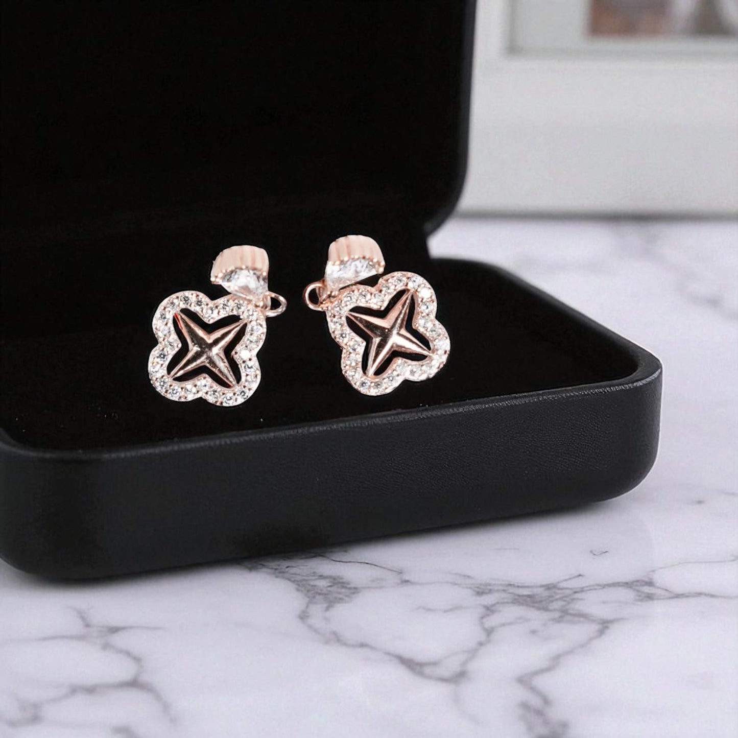 Star-shaped earrings in a black jewelry box on a marble surface