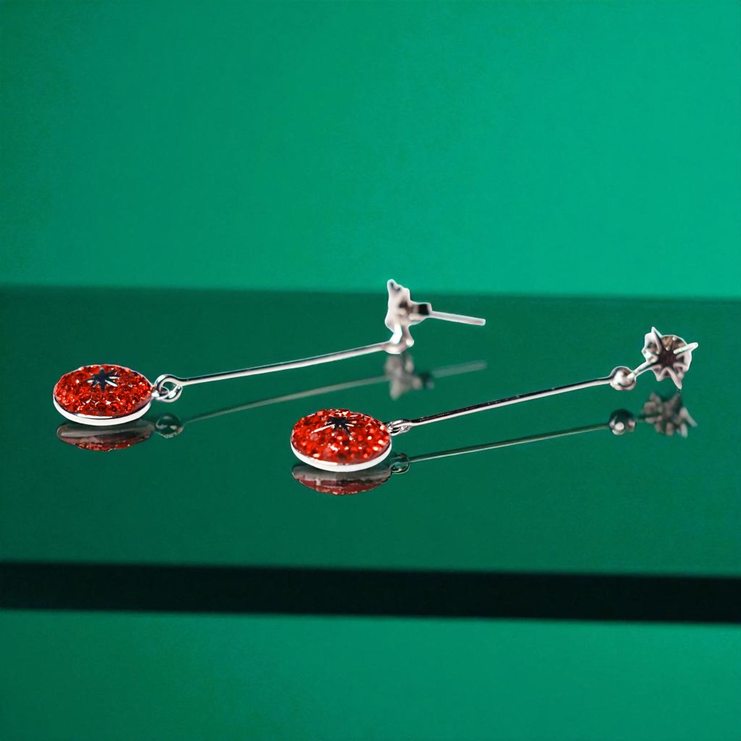 Pair of silver earrings with red gemstones on a green background