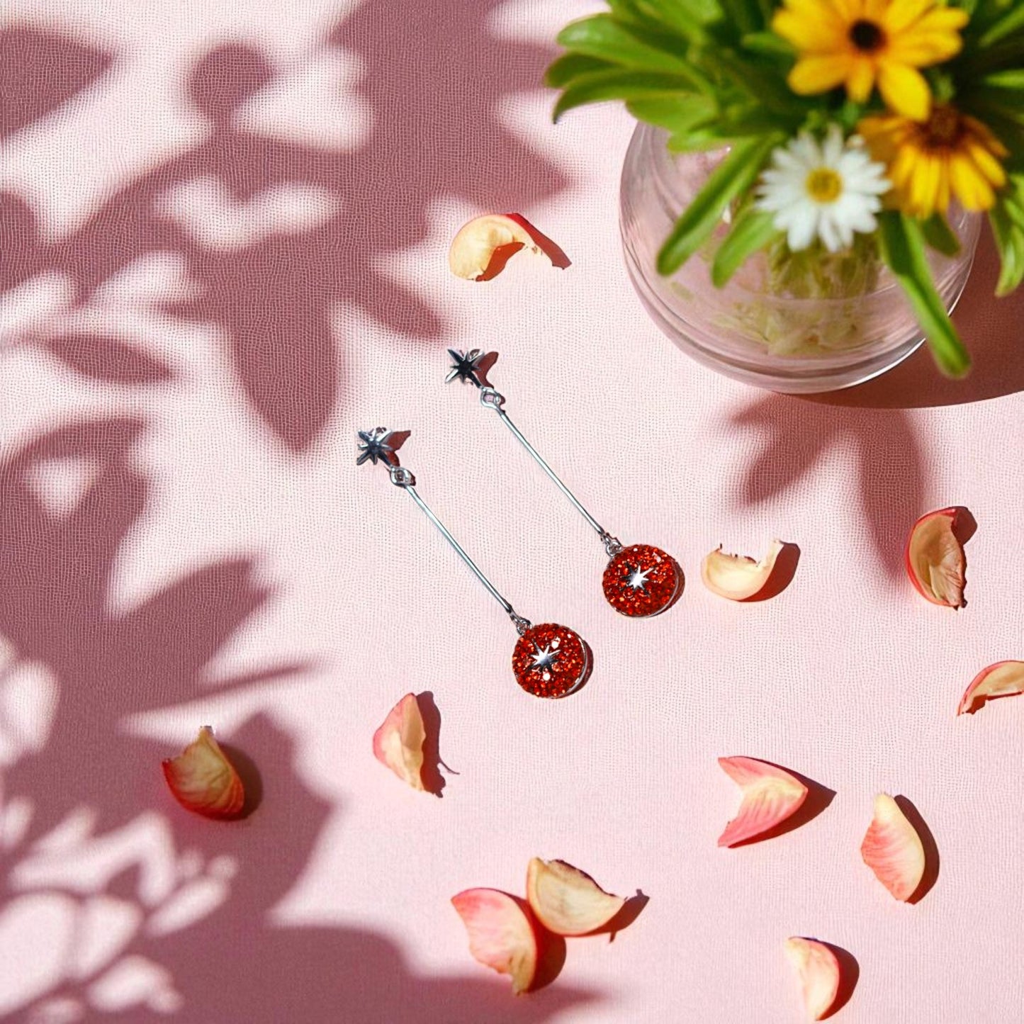 Pair of earrings on a pink surface with flowers and petals