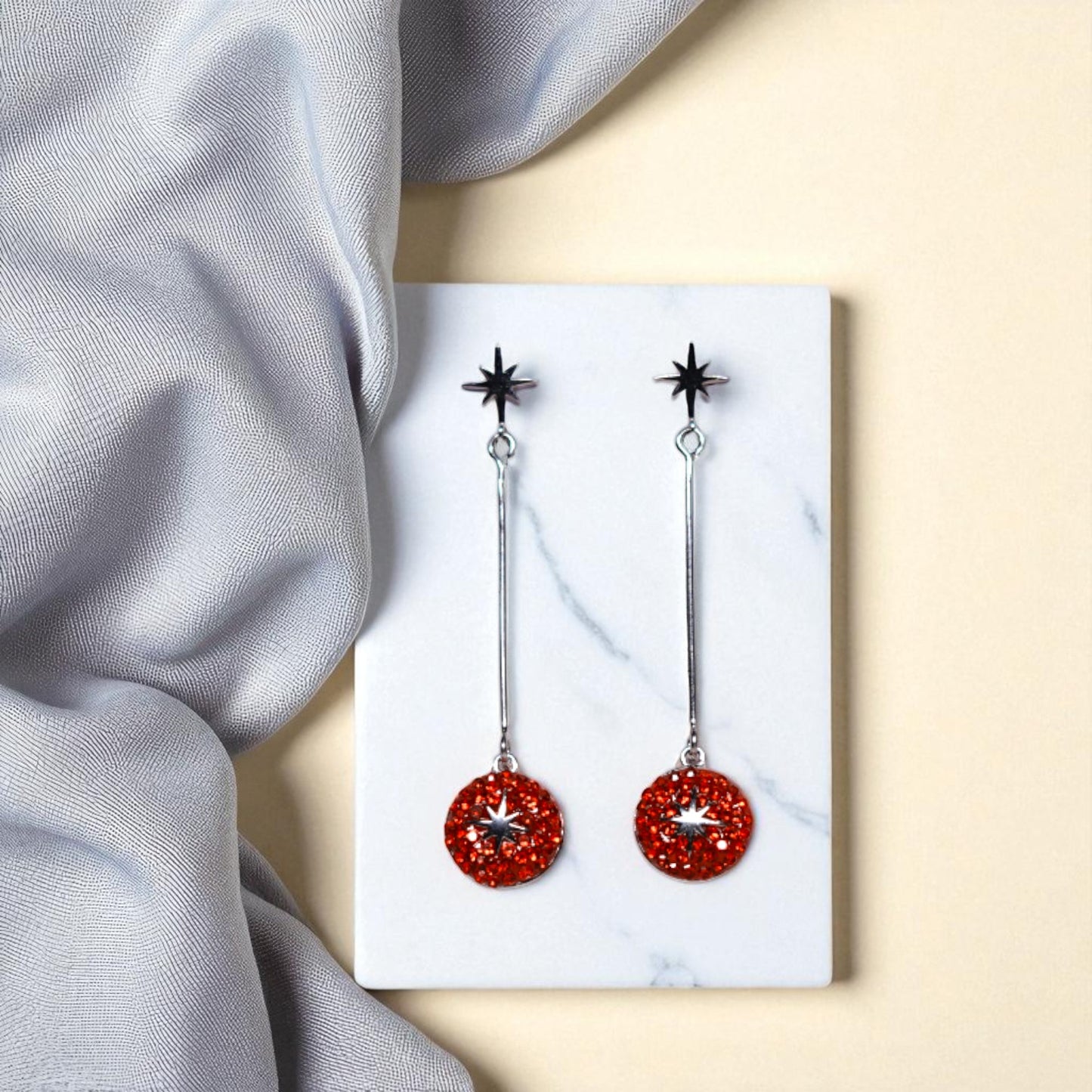Red earrings with star designs on a white card against a light gray fabric background