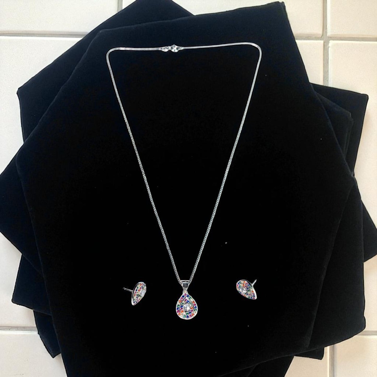 Silver necklace and earrings set on black velvet against a white tiled wall.