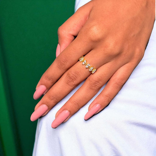 Hand with pink nails wearing a gold ring on a white and green background