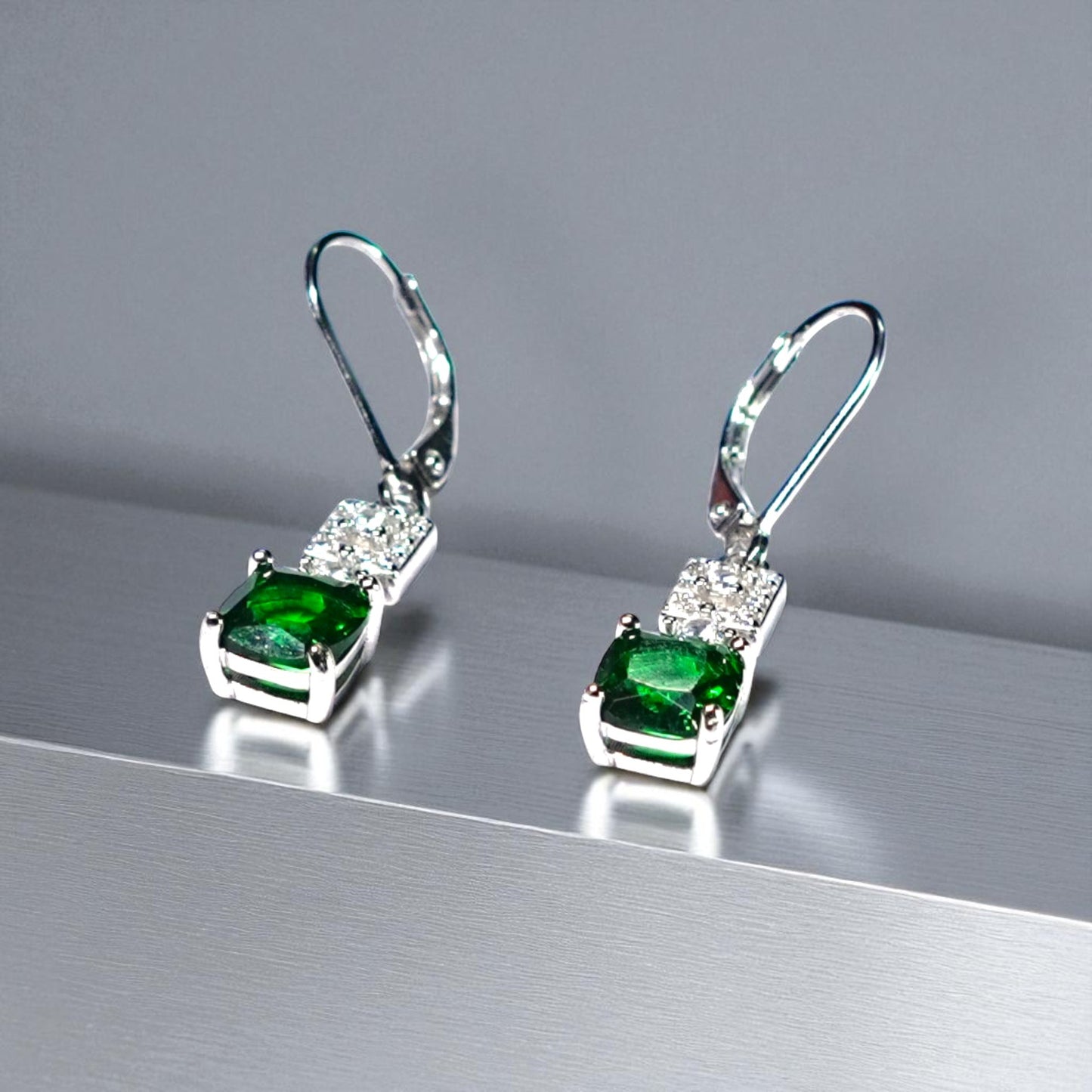 Pair of silver earrings with green gemstones on a reflective surface