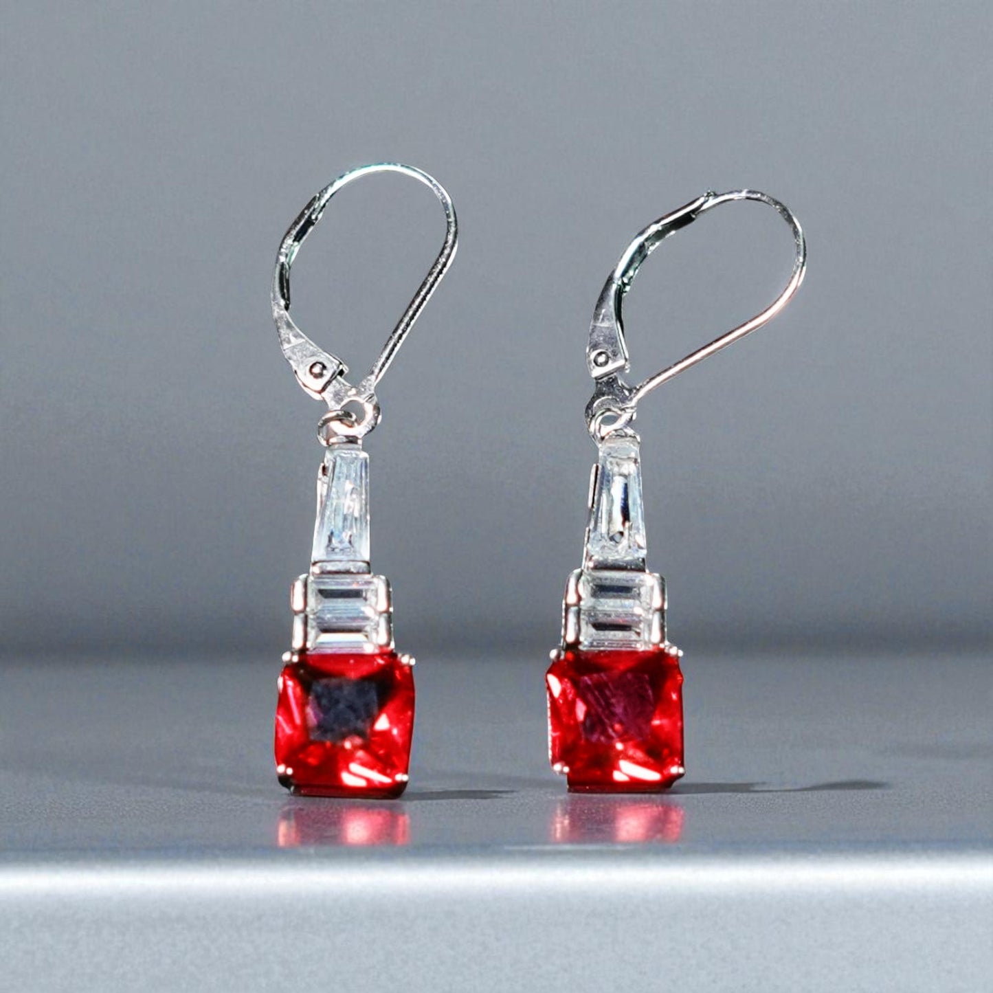 Pair of earrings with red gemstones and silver hooks on a gray background