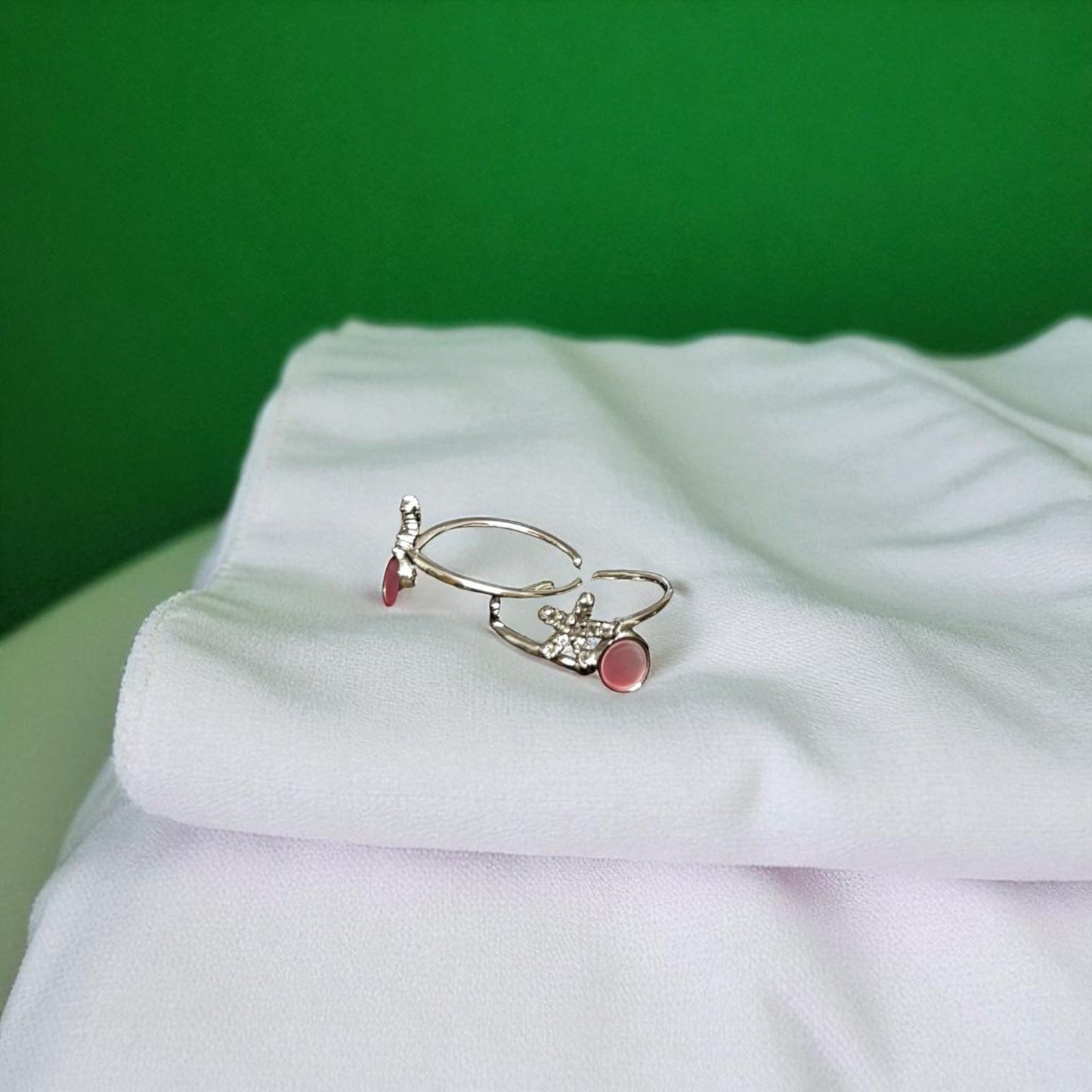 Three rings with gemstones on a white fabric surface against a green background
