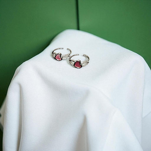 Pair of earrings with red heart stones on a white surface with a green background