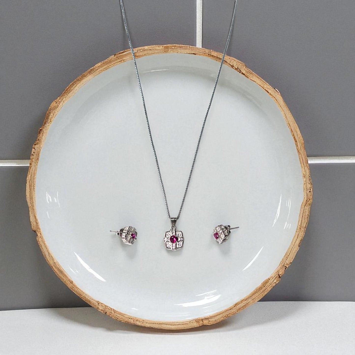 Jewelry set with necklace and earrings on a white plate against a gray background