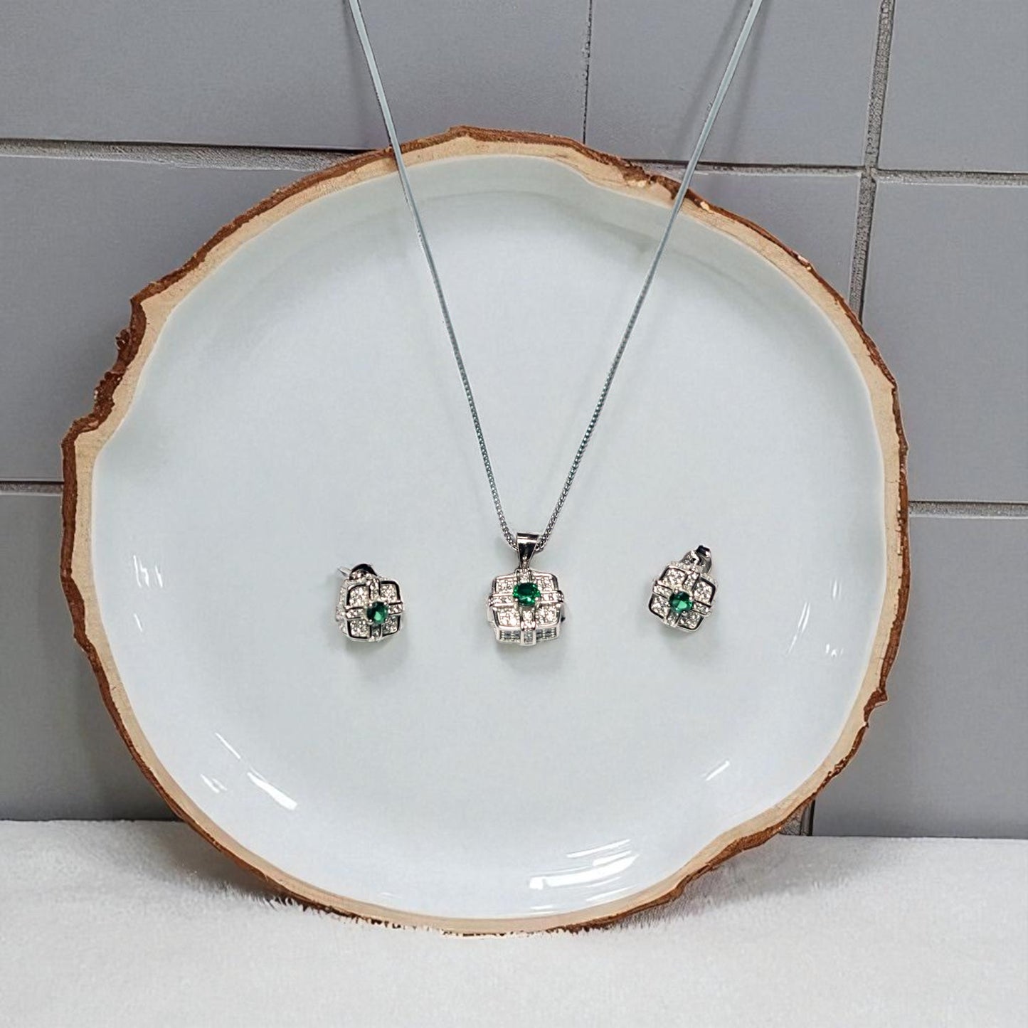Jewelry set with necklace and earrings on a white plate against a tiled wall.
