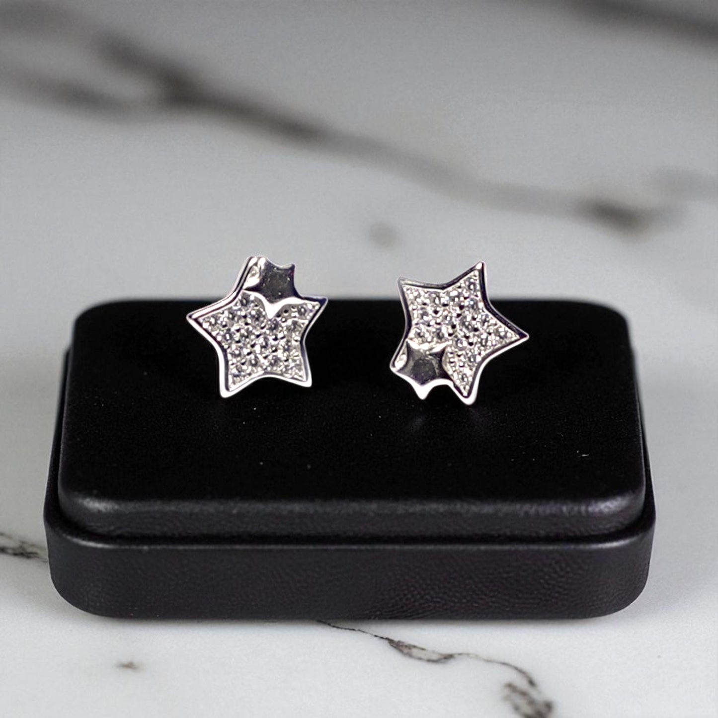 Star-shaped silver earrings with clear stones on a black jewelry box against a marble background