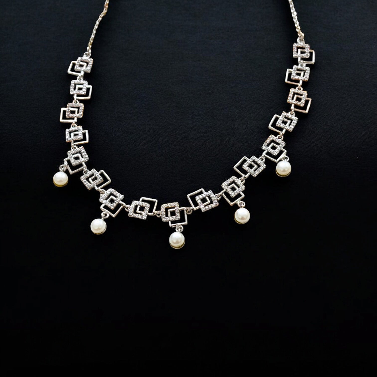 Silver necklace with geometric design and pearl-like beads on a black background