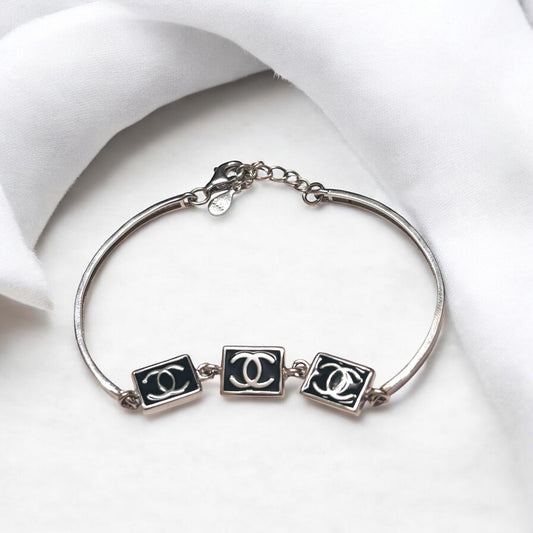 Silver bracelet with three black and white CC logo charms on a white background