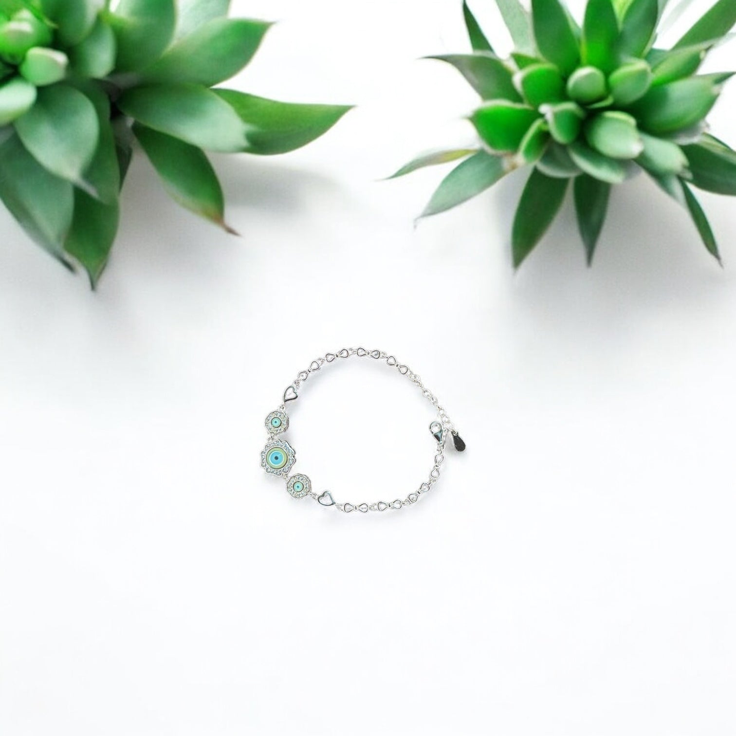 Silver bracelet with green stones on a white background with succulents