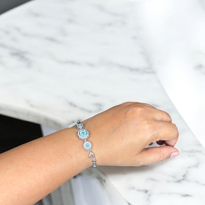Hand wearing a bracelet with blue heart charm on a marble surface