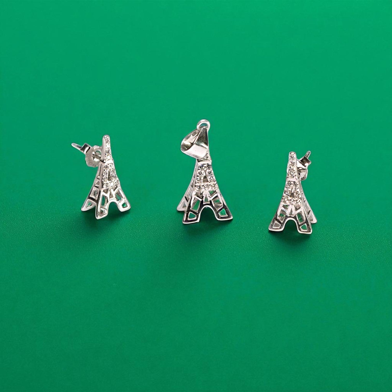 Three silver Eiffel Tower charms on a green background