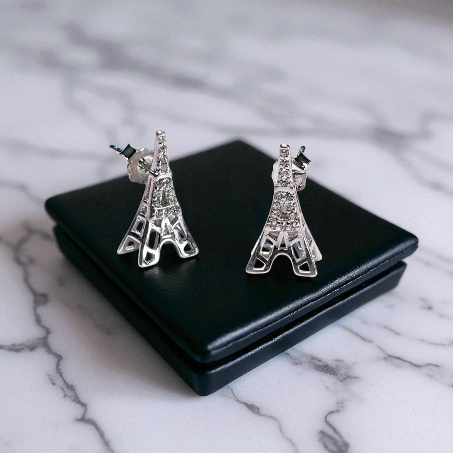 Eiffel Tower-shaped earrings on a black stand with a marble background
