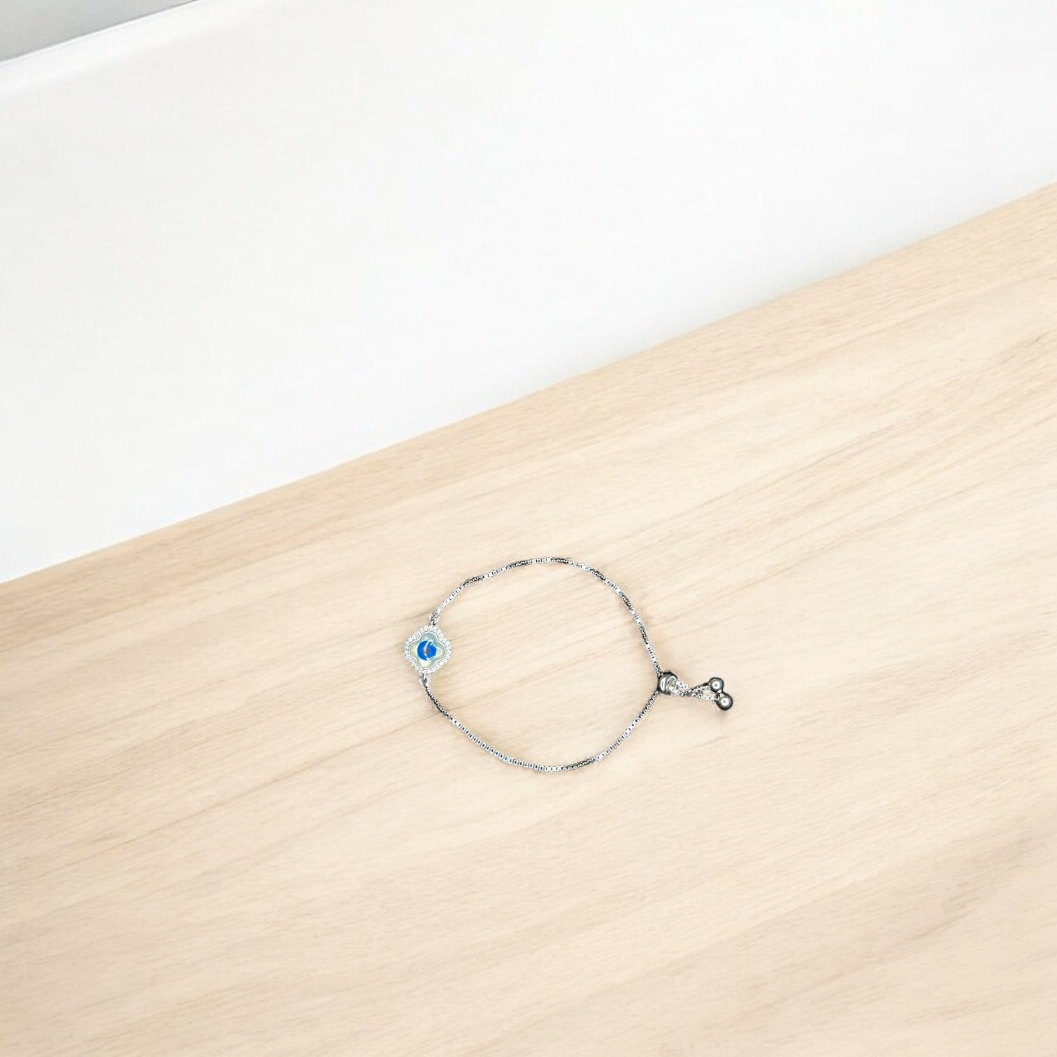 Silver bracelet with a blue evil eye charm on a wooden surface