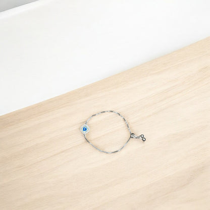 Silver bracelet with a blue evil eye charm on a wooden surface