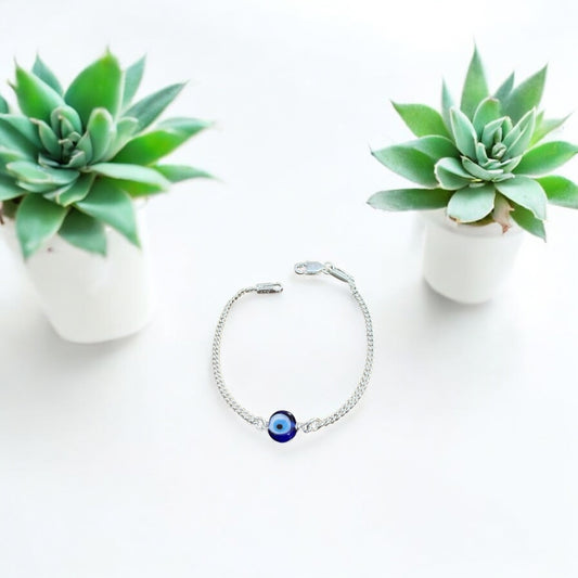 Silver bracelet with a blue evil eye charm on a white background with two succulents.