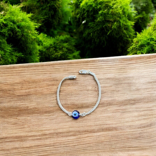 Silver bracelet with a blue eye charm on a wooden surface with greenery in the background