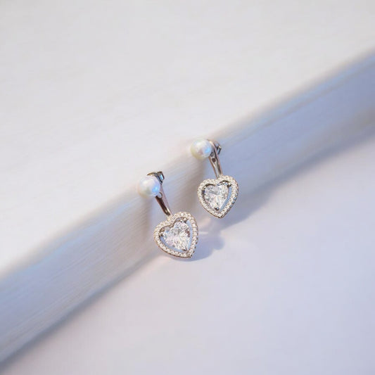 A pair of heart-shaped pearl earrings with silver hoop earrings on a white surface.