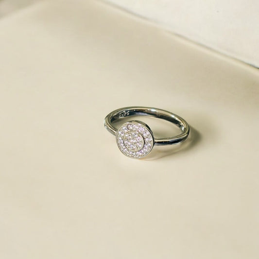 Silver ring with a circular gemstone on a beige background