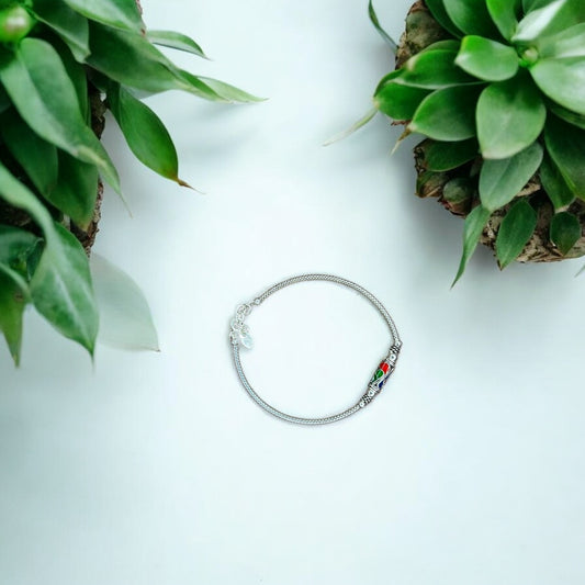 Silver bracelet with colorful beads on a light blue background with green plants.