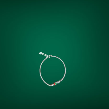 Silver bracelet with a red and green charm on a green background