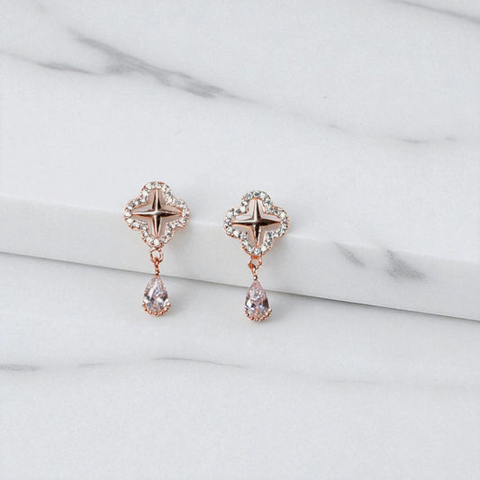 Rose gold earrings with star and teardrop designs on a light gray background