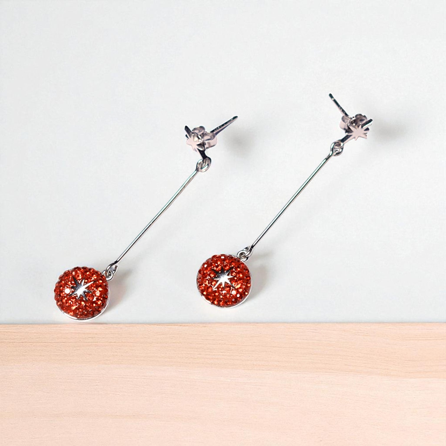 Pair of earrings with red circular charms on a white background
