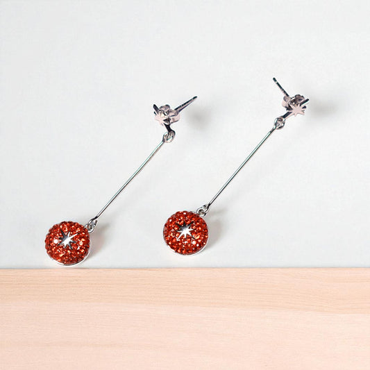 Pair of earrings with red circular charms on a white background