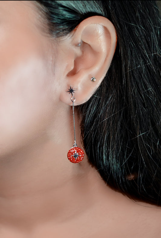 Close-up of an ear with a red floral earring and star-shaped stud.