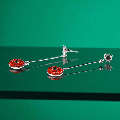 Pair of silver earrings with red gemstones on a green background