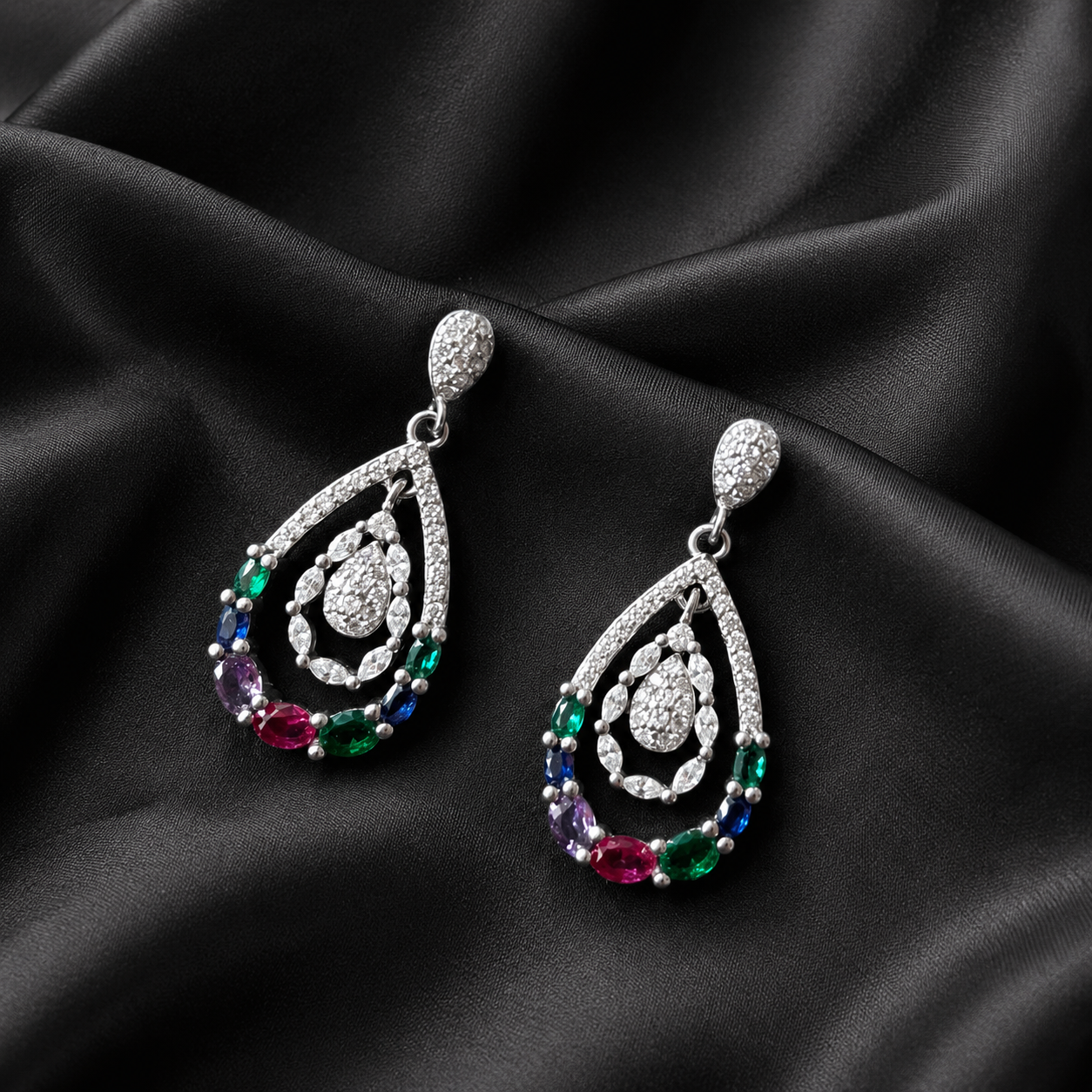 Teardrop-shaped earrings with colorful gemstones on a black satin background