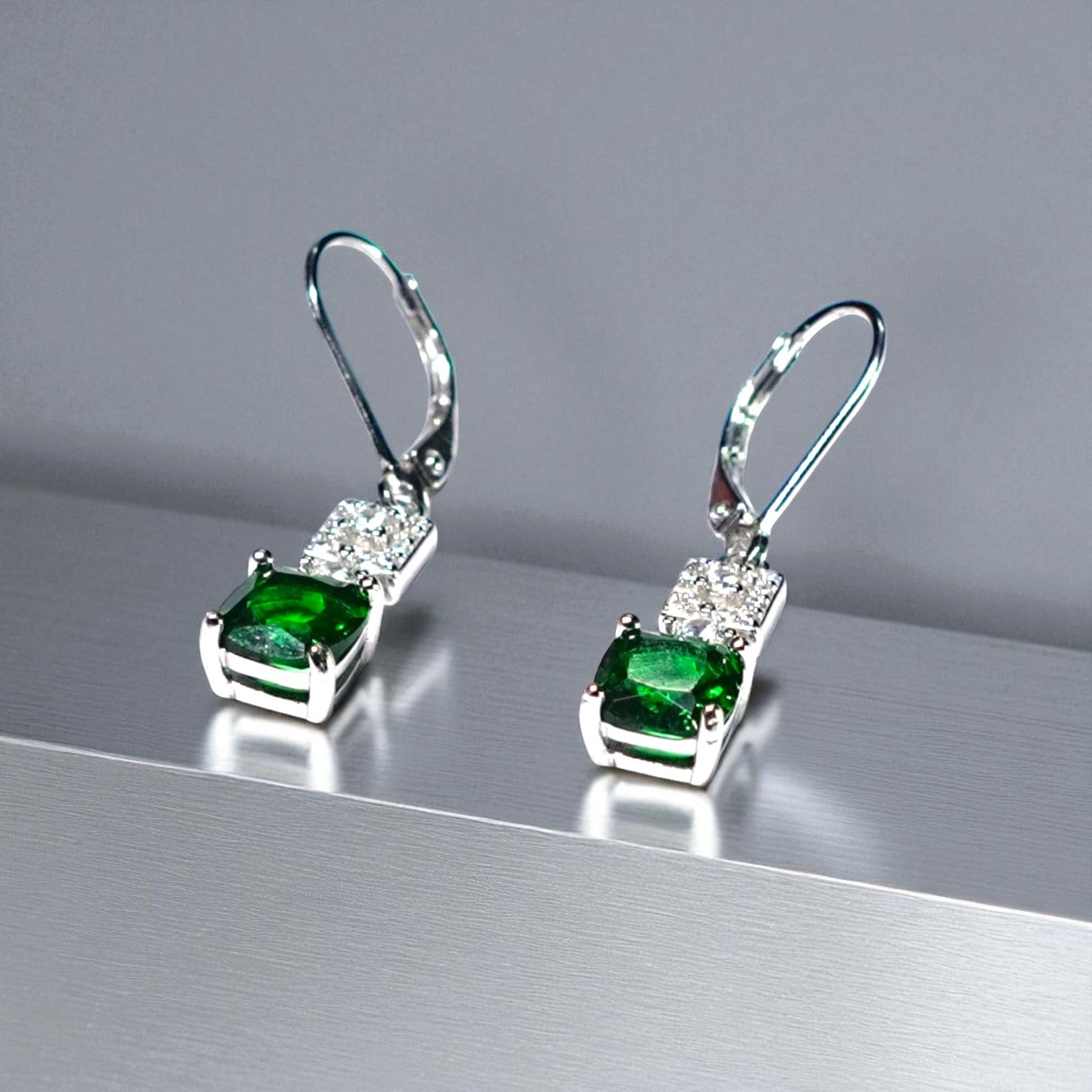 Pair of silver earrings with green gemstones on a reflective surface