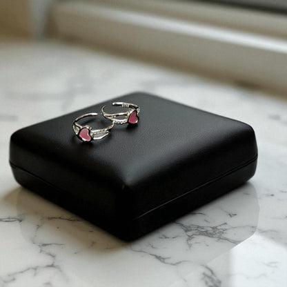 Pair of silver earrings with pink heart details on a black case against a marble background