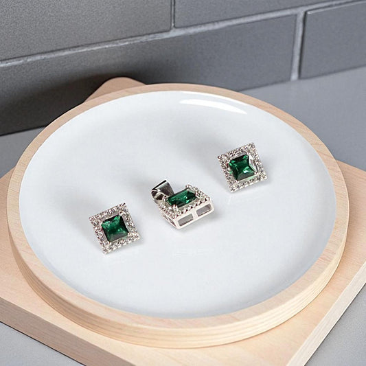 Green gemstone earrings on a white circular stand with a wooden base.