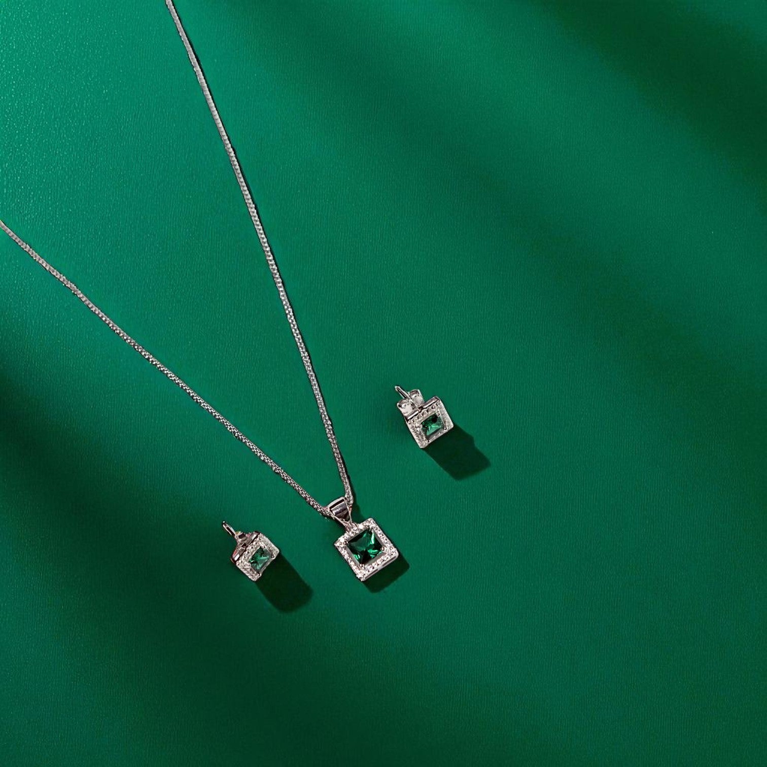 Jewelry set with square emerald stones on a green background